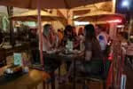 Três mulheres aparecem sentadas na mesa de um bar